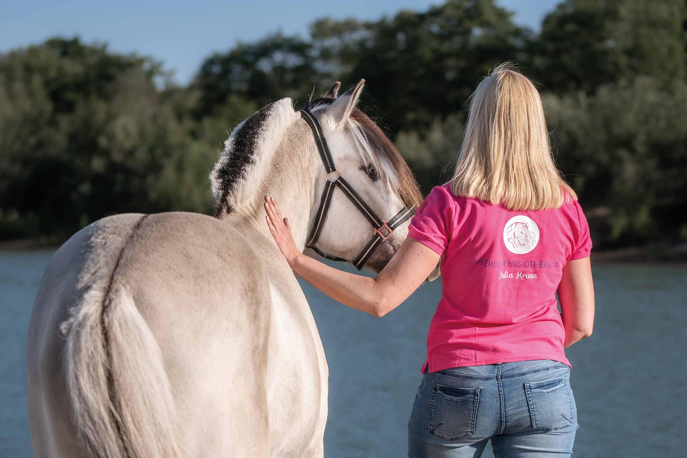 Julia steht mit ihrem Pferd an einem See - Julia Kruse, Pferdephysiotherapie
